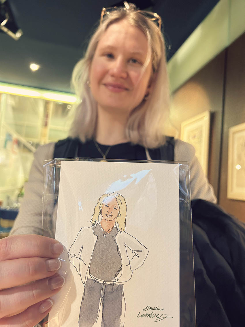 Visiteuse tenant son portrait à l’aquarelle réalisé en direct pendant un vernissage au musée.